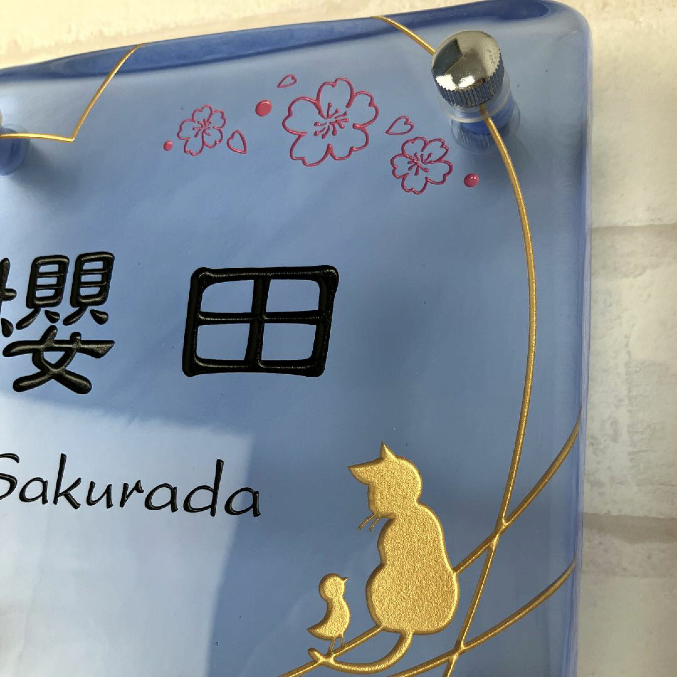 ブルーの手作りガラス表札。文字は黒色。ハート、猫、小鳥のデザインはゴールド、桜のデザインはピンク色。
