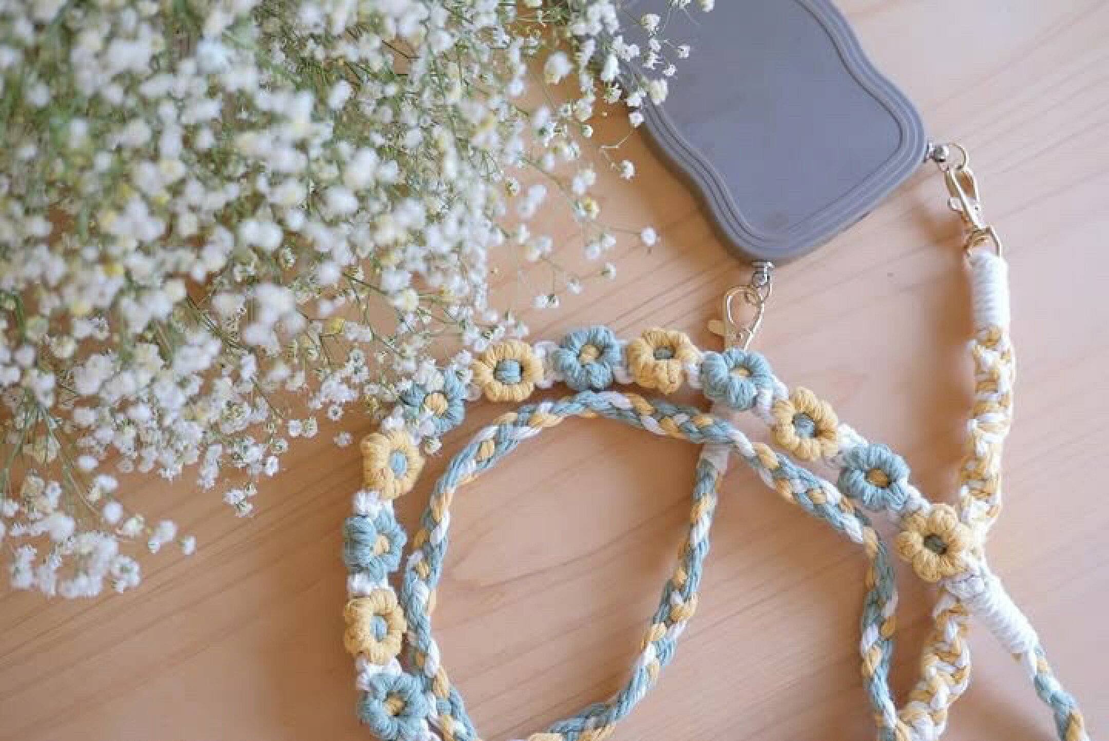 マクラメ糸を使用したスマホショルダーです。ブルーやイエロー系を使用して優しい感じに仕上げました。平編みなどの編み方をいくつも作ることで個性的なデザインになるように仕上げました。コットンならではの優しさを生かしています。お花も可愛い。