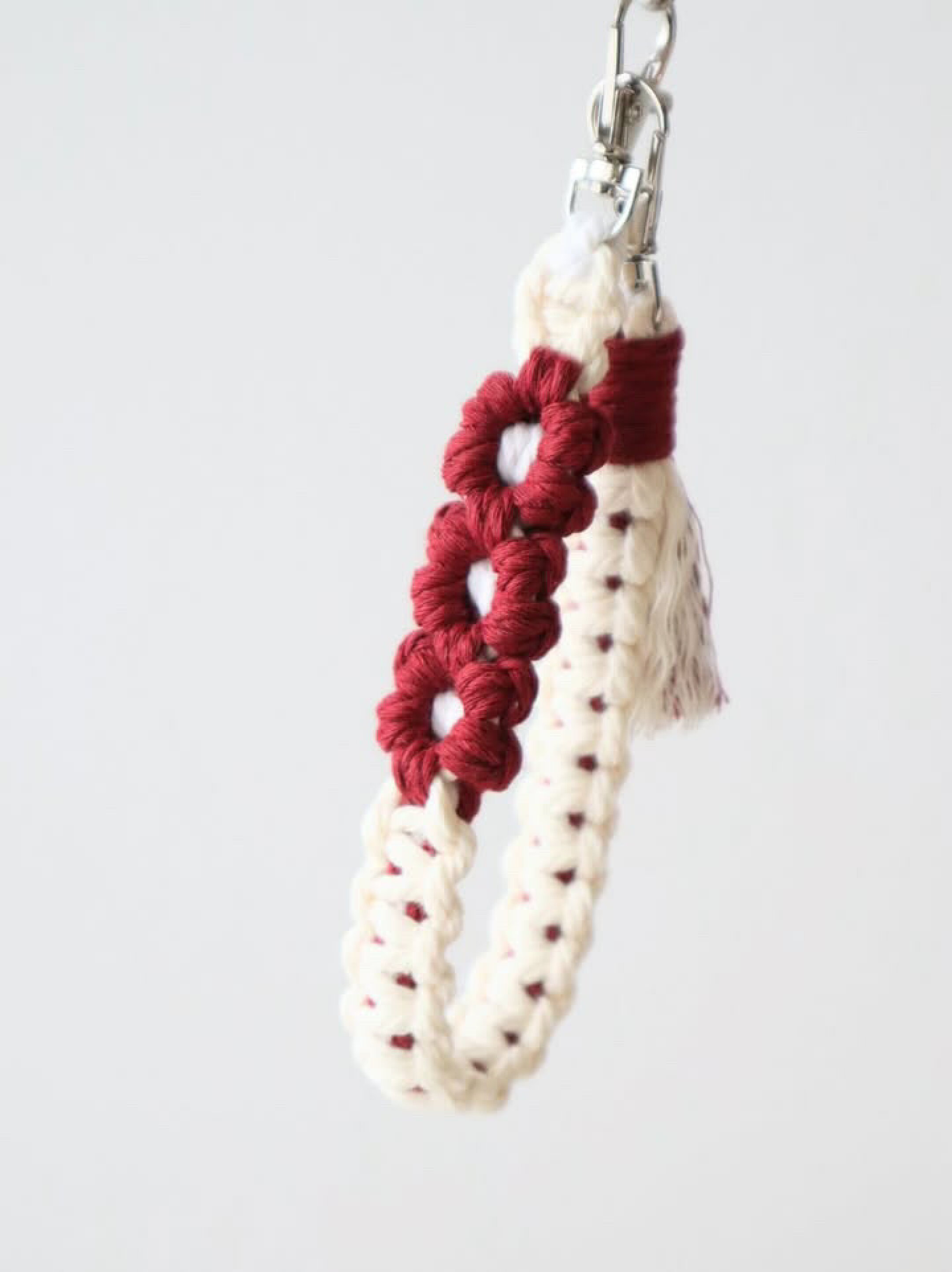 お花編みとフリンジが可愛いスマホストラップです。ホワイト系２色とレッド系を組み合わせて作成していただきました。柔らかな印象になるマクラメ糸なのでカラーに強弱を付けてもなじみやすい作品に仕上がります。柔らかいのでタッセルなどのフリンジ作成もしやすいです。