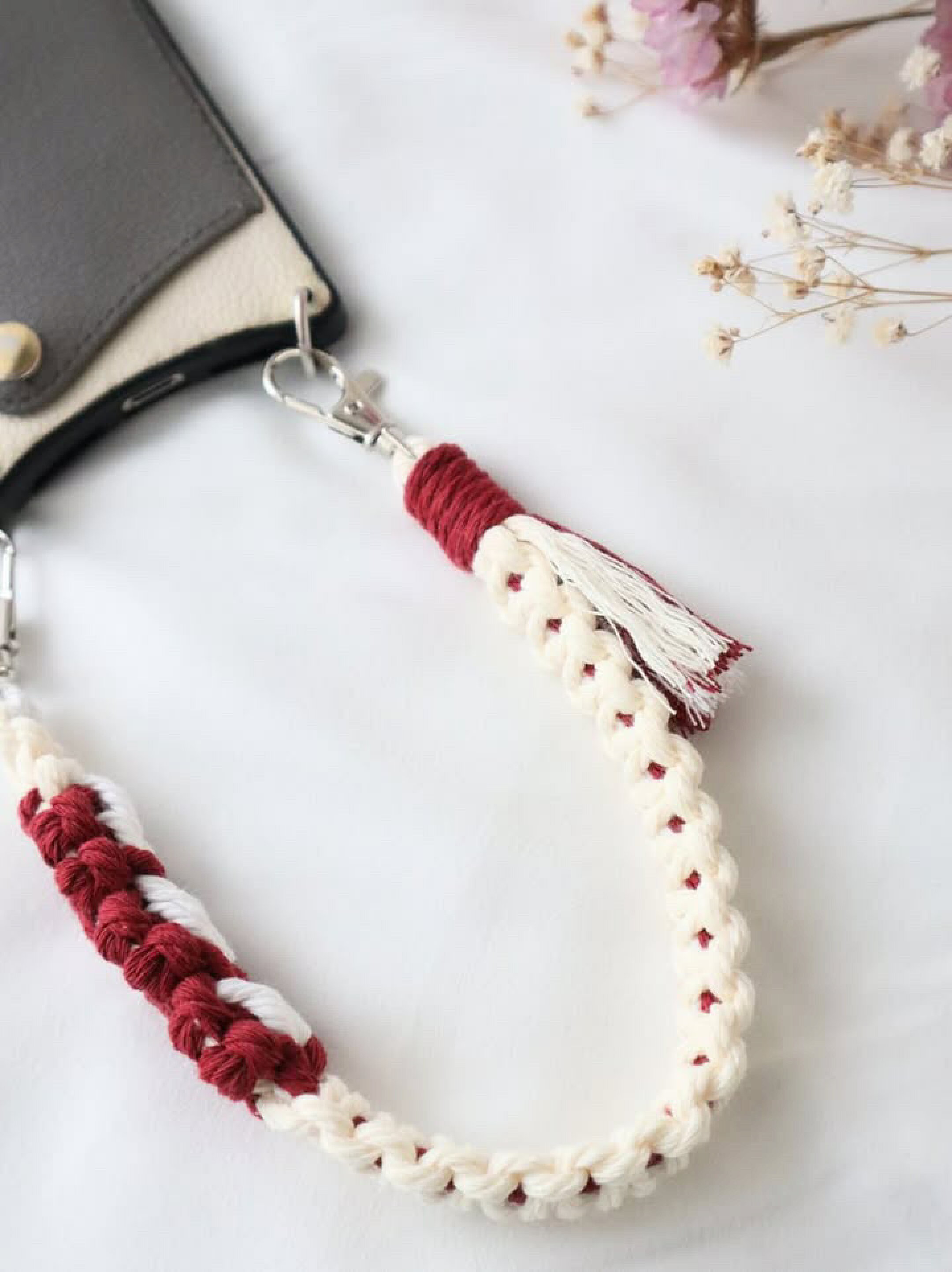 お花編みとフリンジが可愛いスマホストラップです。ホワイト系２色とレッド系を組み合わせて作成していただきました。柔らかな印象になるマクラメ糸なのでカラーに強弱を付けてもなじみやすい作品に仕上がります。柔らかいのでタッセルなどのフリンジ作成もしやすいです。
