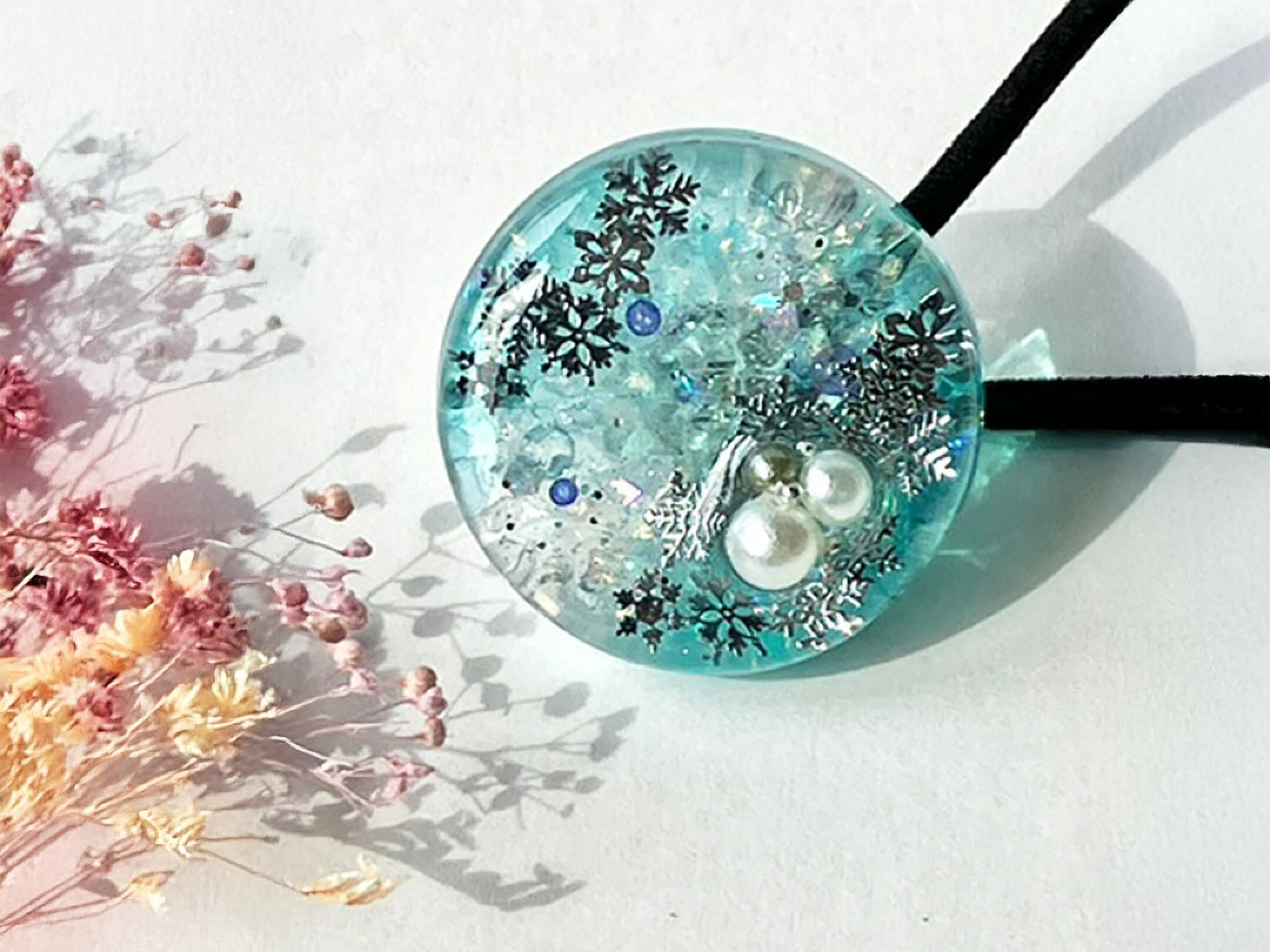 透明感あふれるブルーの中に、波のきらめきや舞い上がる砂のような粒子、パールやスノーフレークモチーフを閉じ込めたレジンアクセサリー。素材一つひとつが繊細に重なり合い、まるで静かな海辺や冬の空気を思わせる癒しの世界が広がります。