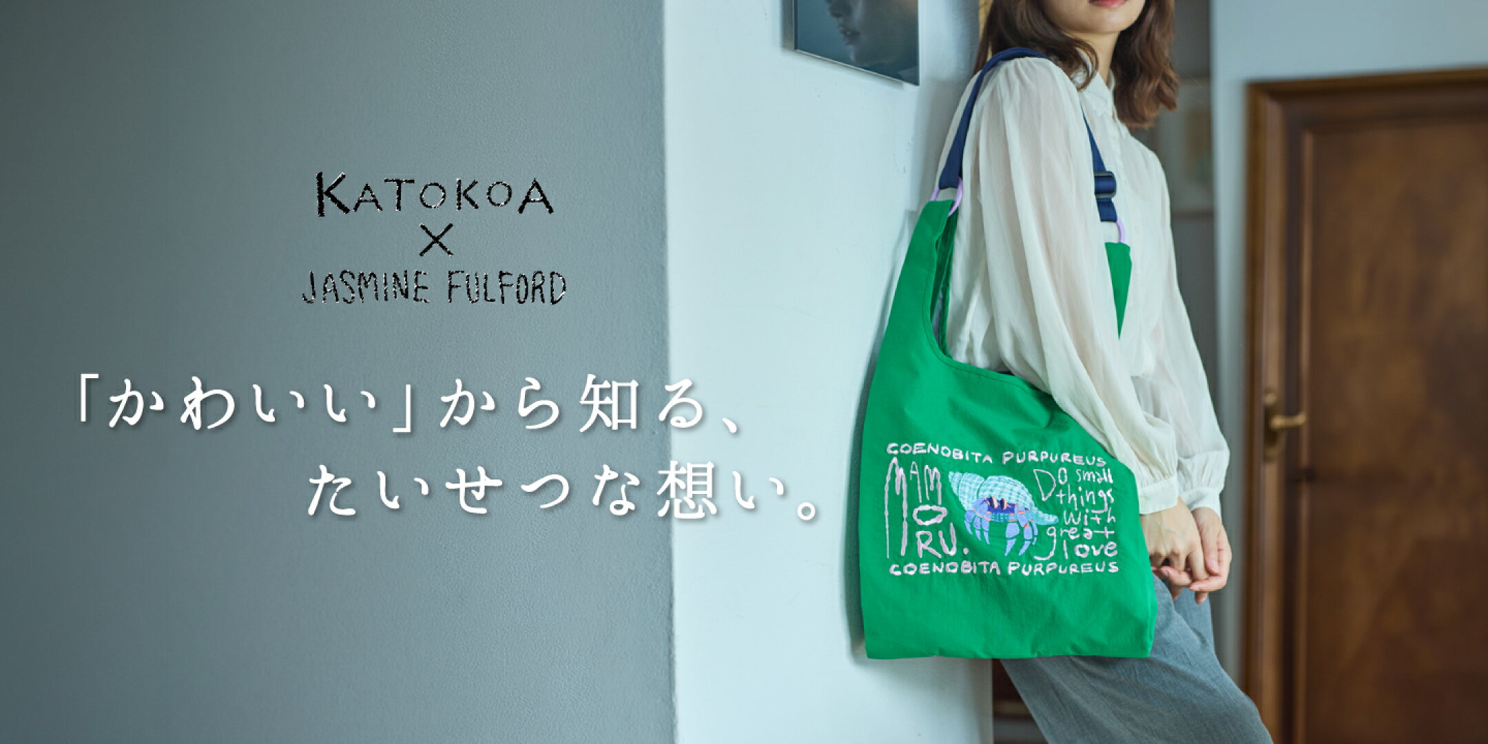 ヤドカリが刺繍されたグリーンのバッグを肩に掛けて壁にもたれる女性
