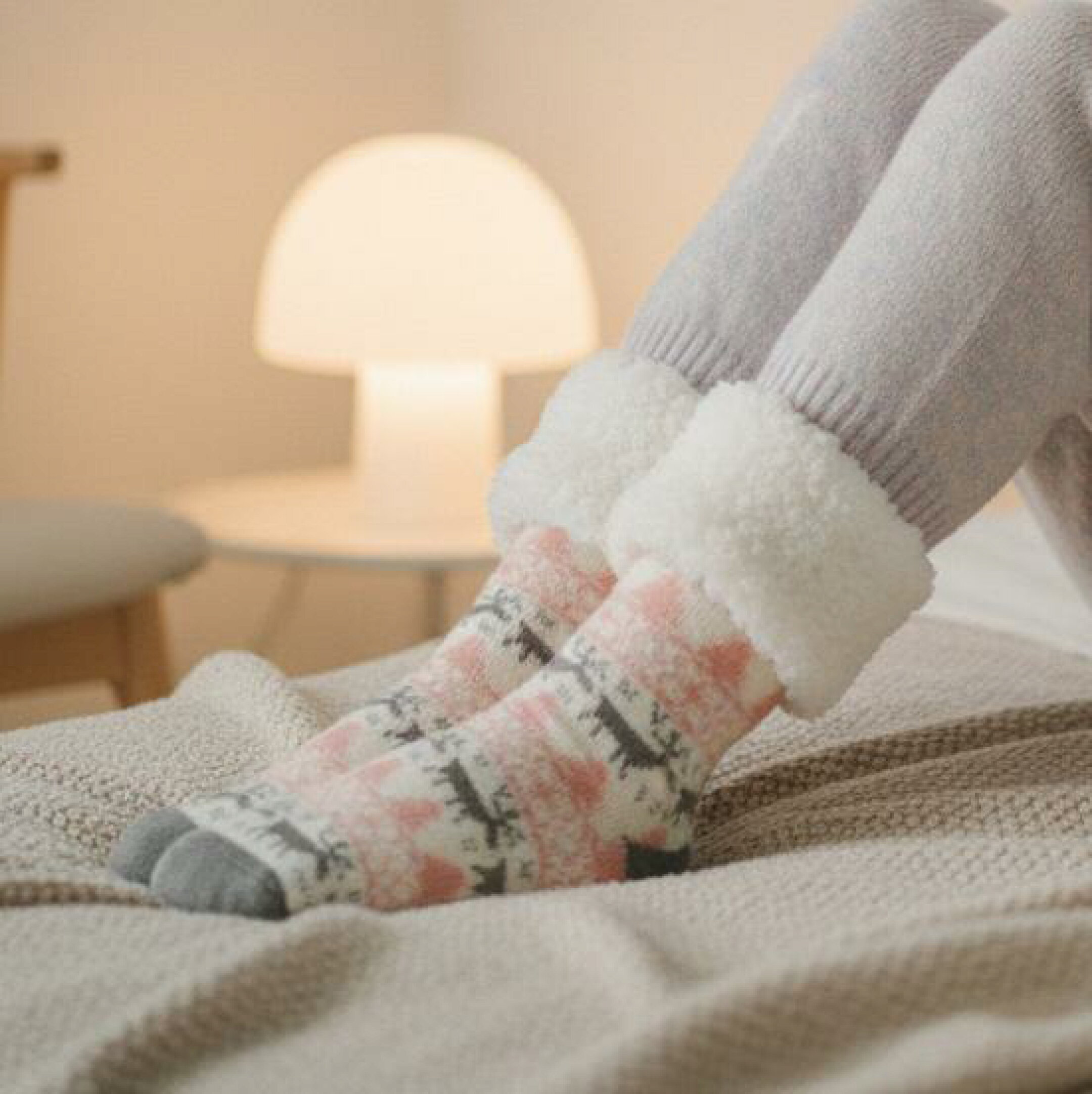 ARUONの極厚裏ボアルームソックス。ピンク×グレーのトナカイ柄。寝室の柔らかな照明の中でリラックスする就寝前シーンを表現。